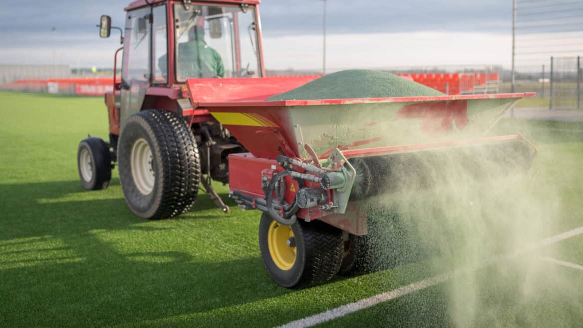 tractor applying silica infill to artificial grass during an installation